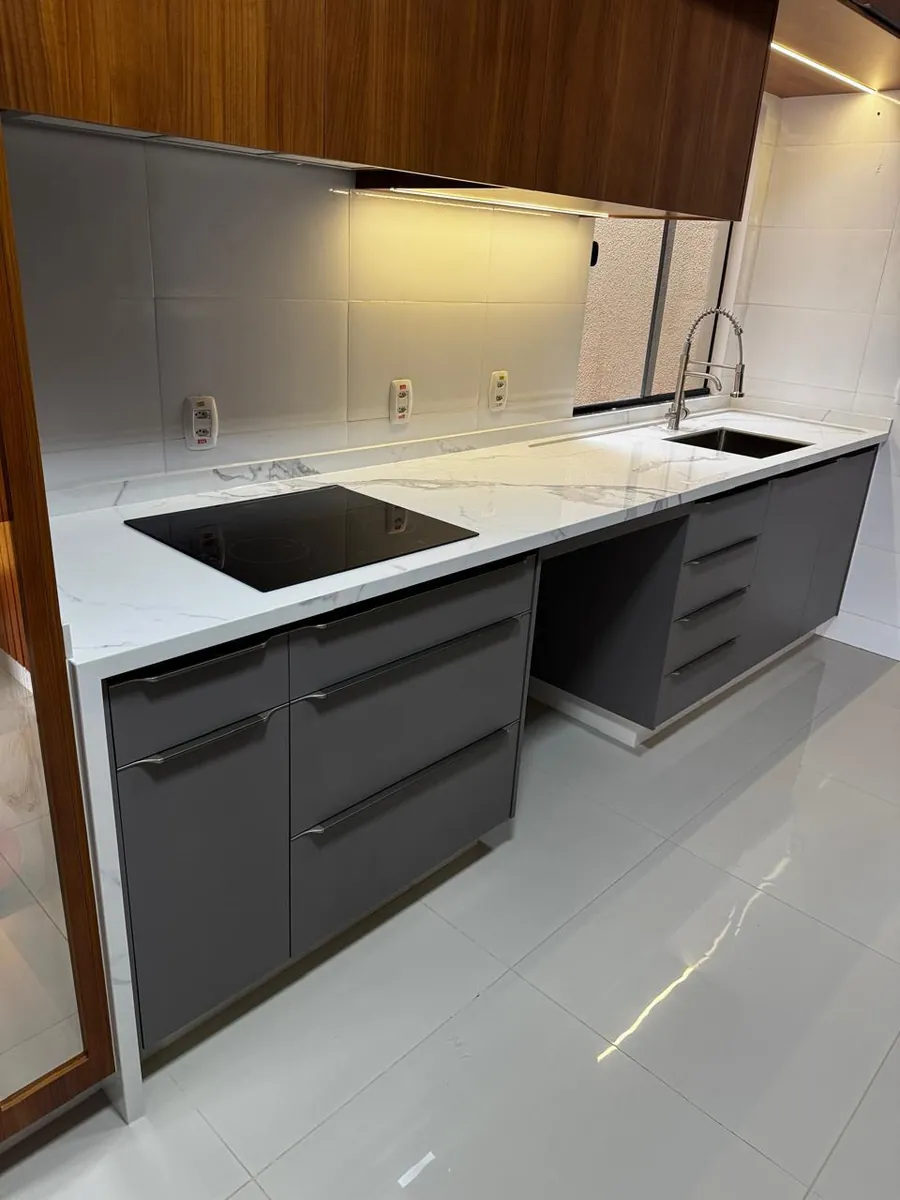 Bancada de cozinha em pedra branca com cooktop e armários planejados