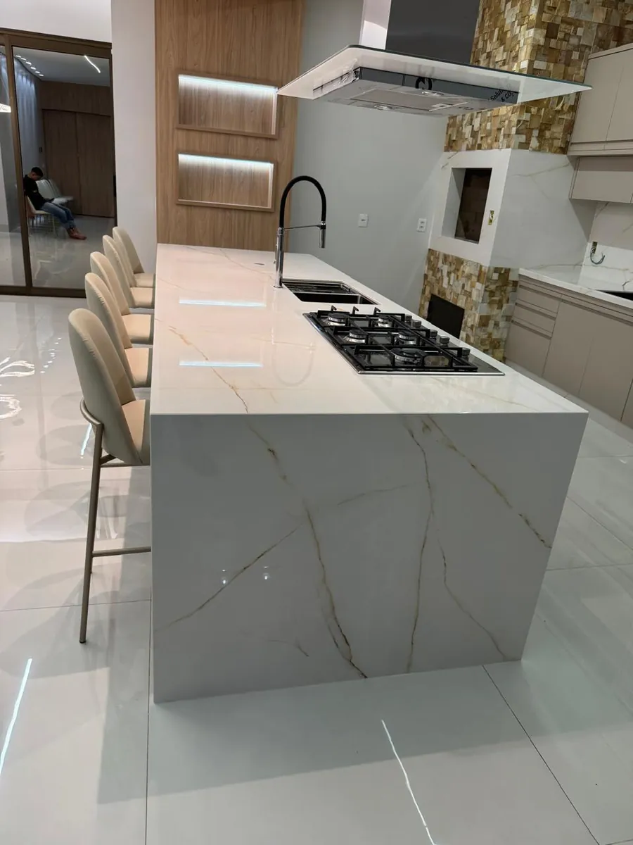 Ilha de cozinha em mármore branco com cooktop e revestimento de pedra ao fundo